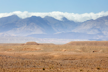 Fototapeta na wymiar stone desert with mountains peaks and clouds in Morocco