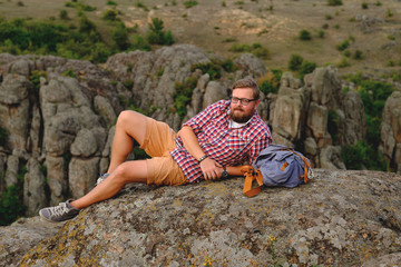 young man with a beard sitting on canyon cliff