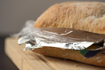 Fresh tasty panini sandwich with plastic waste and paper cardboard inside on wooden board. Recycled waste in our food concept