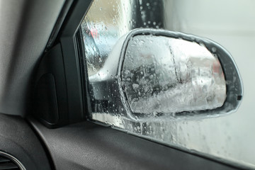 View from inside the car, looking at side mirror, wet from water and soap when being washed in carwash.