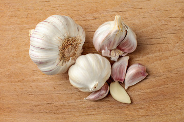 Table top view on garlic bulbs, purple cloves, some of them peeled, on old cutting board.