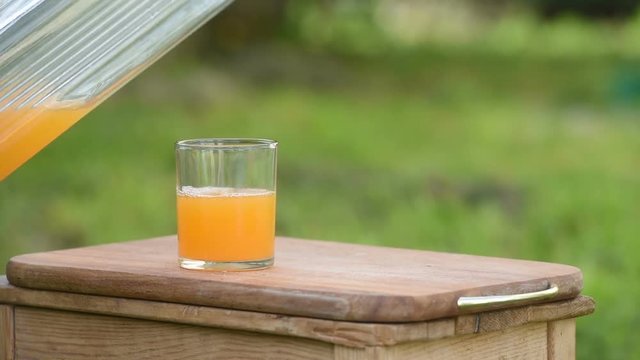 The juice is poured into a glass on a background of green nature