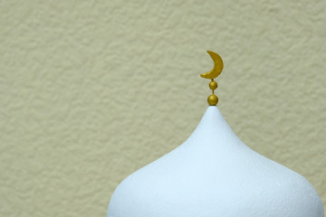 A close-up of the symbol of Islamic culture and religion. A crescent of gold color is handmade on a white minaret. Light background.