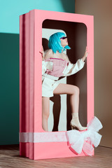 fashionable beautiful girl in blue wig posing in decorative pink box with bow