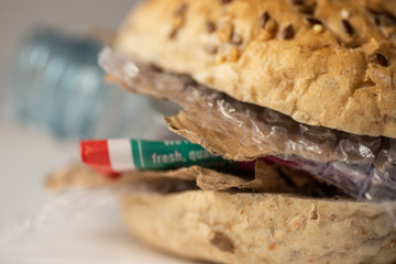 Fresh tasty burger with plastic waste and paper cardboard inside on white background. Recycled waste in our food concept