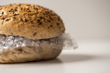 Fresh tasty burger with plastic waste and paper cardboard inside on white background. Recycled waste in our food concept