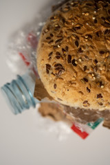 Fresh tasty burger with plastic waste and paper cardboard inside on white background. Recycled waste in our food concept