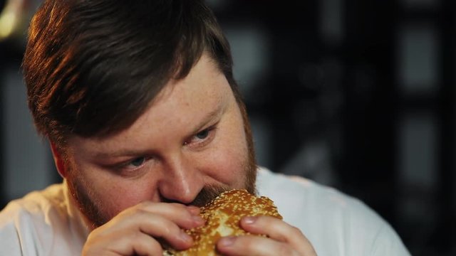 Fat man watches TV and eats a burger