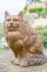 Close-up of a terracotta cat resting on a wall. Selective focus and blurred background.