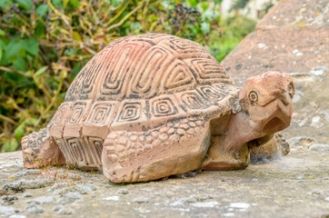 Close-up of a terracotta turtle resting on a wall. Selective focus and blurred background.