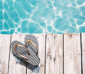 Summer flip-flops on a wooden platform by the edge of the pool against water background. Photo...