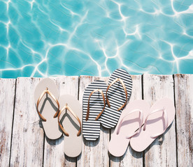 Summer flip-flops on a wooden platform by the edge of the pool against water background. Photo...