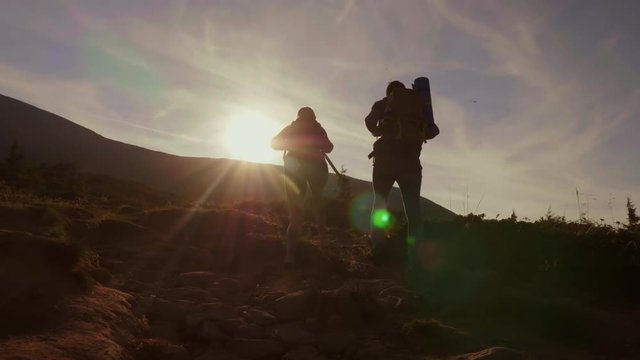 Climbing The Mountain At Dawn. Two Tourists Climb Up The Mountain Path In The Sun