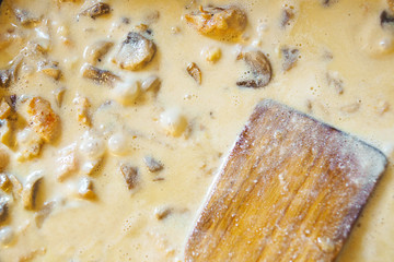 Grated cheese on chicken with mushrooms in sour cream sauce in a frying pan with a wooden spoon