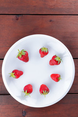 Strawberries on a white plate top view, red berries on a wooden background, fresh strawberries on dark wooden boards, vegetarian food, copy space