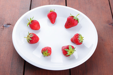 Strawberries on a white plate top view, red berries on a wooden background, fresh strawberries on dark wooden boards, vegetarian food, copy space