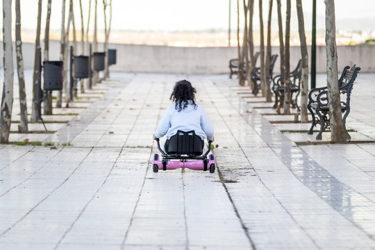 Hoverboard o pat&iacute;n el&eacute;ctrico con sill&iacute;n manejado por una ni&ntilde;a morena rizosa mientras juega en el barrio