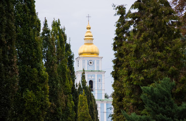 The dome with the cross and the clock of the Christian Church surrounded by a corridor of trees - green coniferous arborvitaes