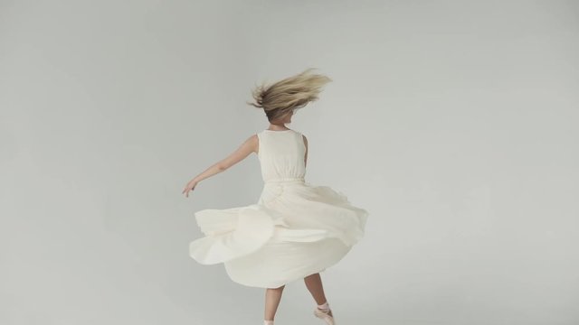 The ballerina is spinning in dance on tiptoes in pointe shoes. ballet dancer in a light fluttering dress. young attractive girl is dancing on a white background