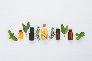 Bottle of essential oil and herbal medicine with fresh herbs sage, rosemary, mint and spearmint setup with flat lay on white wooden table. top view