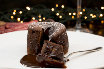 CHOCOLATE MOLTEN LAVA CAKE DECORATED WITH ICING SUGAR ON A WHITE PLATE AND CHRISTMAS LIGHTS BACKGROUND