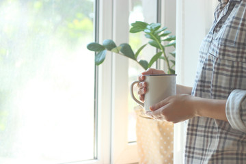 a cup of tea or coffee in female hands on the window background. Morning, pajamas, minimalism. insta