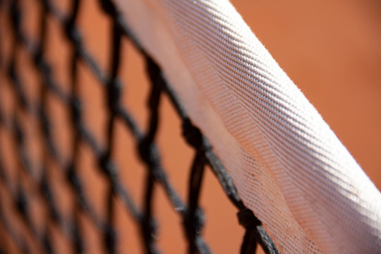 Detailaufnahme eines Tennisnetzes mit Sandplatz im Hintergrund