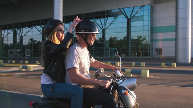 Happy young couple riding vintage scooter on urban background and having some fun, slow motion