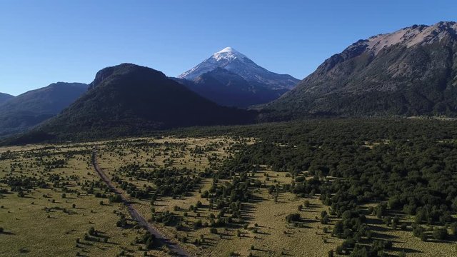 Aerial drone Scene of mountains, trees and a dirt road, Piedra Mala, Lanin volcano with snow, Paimun lake, Neuquen, Patagonia, Argentina. Camera moving forwards.
