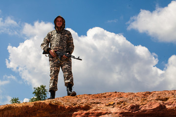 man in camouflage uniform with a weapon in the desert.