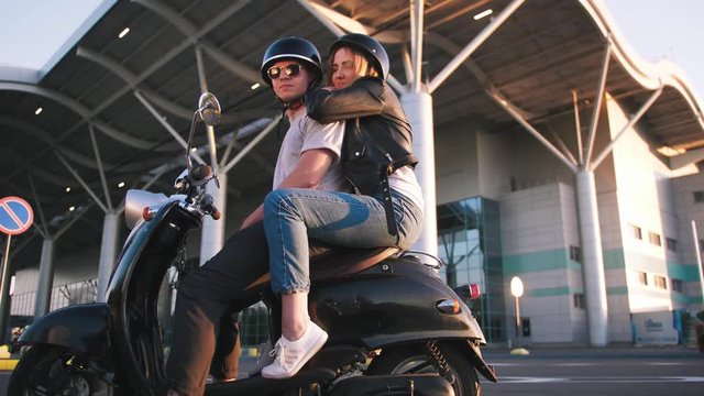 Happy young couple riding vintage scooter on urban background and having some fun, slow motion