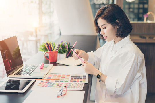Young woman designer choosing colored pencils and color samples sheets for selection on office desk.