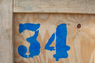 The number 34 is written in blue paint on a wooden box. The number for cargo transportation. Careless inscription. Printing on fabric and fashionable clothes. © mangz