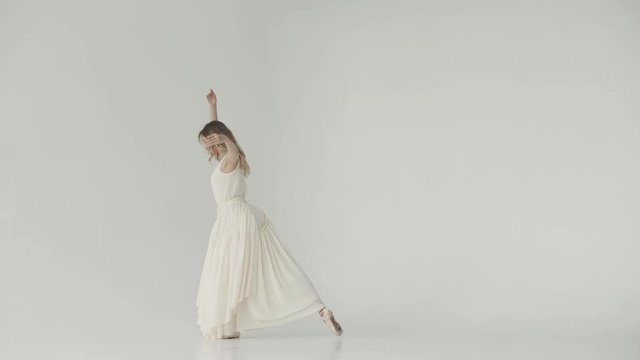 ballerina in a light studio dances in pointe shoes. ballet dancer in a light fluttering long dress