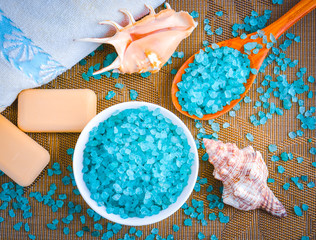 Blue sea salt for spa treatments in a white vase on the background of a shell, a towel and a wooden...
