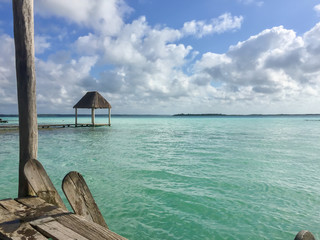 View from a dock over the clear waters of Lago Bacalar in Mexico with a small tiki hut