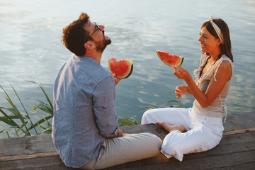 Young couple eating watermelon by the river during the sunset