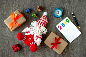 Santa Claus and gifts for the new year 2019. Funny Santa Claus, gifts, paper notebook, clock and figures 2019 on a gray wooden background. Plans for the new year.