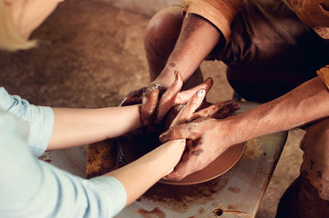 Hands of two people create pot on potter's wheel. Teaching pottery, carftman's hands guiding
