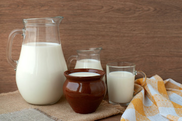 Milk in different dishes. Milk jugs, a glass and a clay pot in a rustic style. A lot of milk on sacking.