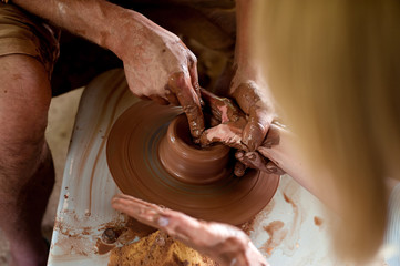 The potter is molding from clay on a potter's wheel. The hands of the potter