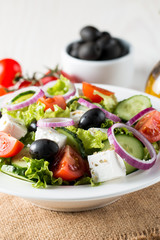 Fresh Greek salad made of cherry tomato, ruccola, arugula, feta, olives, cucumbers, onion and spices. Caesar salad in a white bowl on wooden background. Healthy organic diet food concept.