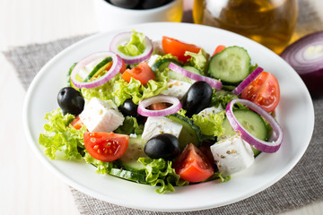 Fresh Greek salad made of cherry tomato, ruccola, arugula, feta, olives, cucumbers, onion and spices. Caesar salad in a white bowl on wooden background. Healthy organic diet food concept.
