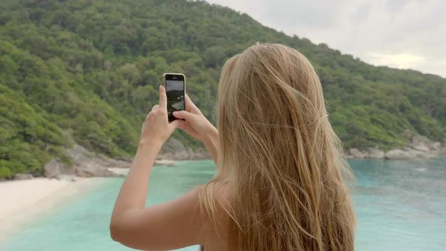 Rear slow motion shot of young blonde woman taking picture of landscape with her smartphone. Tourism, technology, vacation and leisure concept.