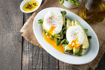 Avocado toast, cherry tomato on wooden background. Breakfast with toast avocado, vegetarian food, healthy diet concept. Healthy sandwich with avocado and poached eggs.