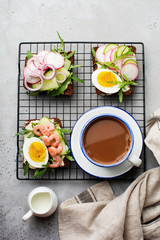 Fototapeta na wymiar Open sandwiches on dark rye bread with eggs, shrimps, radishes, cucumber, cream cheese and arugula for breakfast. Smorrebrod Traditional dish of Danish cuisine. Top view.