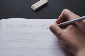 Close-up view of the female's hand writing music notes in the blank music sheets. Concept of the education in arts, music, creativity, music notes writing.