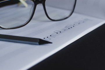 Side view of the pencil and eyeglasses laying on the blank music sheets. Concept of the education in arts, music, creativity, music notes writing.