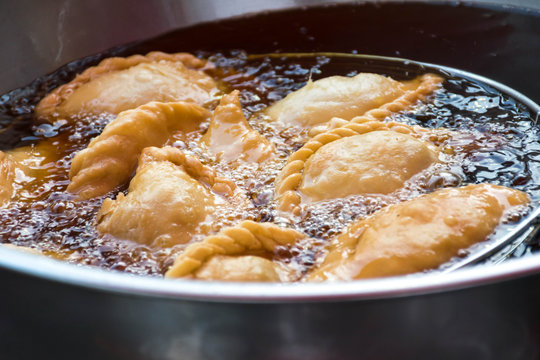 Curry puffs are being fried in a stainless steel pot.