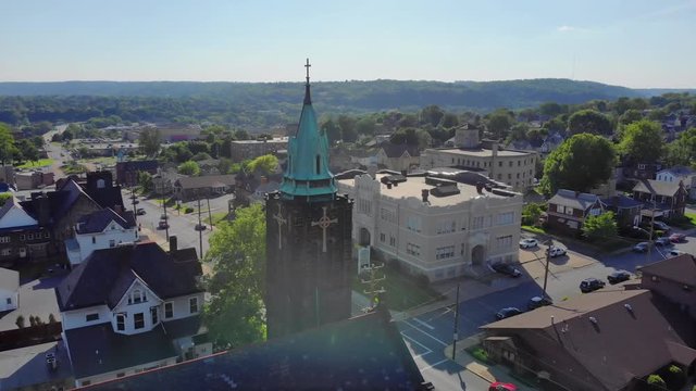 A slow morning or evening aerial approach to a church steeple in a small town's business district. Pittsburgh suburbs.  	